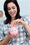 Cheerful businesswoman saving money in a piggy-bank at her desk