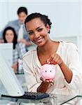 Smiling businesswoman saving money in a piggy-bank at her desk