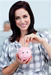Charismatic businesswoman saving money in a piggy-bank at her desk