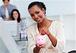 Confident businesswoman saving money in a piggy-bank at her desk