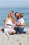 Cute children and their parents sitting on the sand at the beach