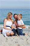 Happy children and their parents sitting on the sand at the beach