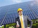 Portrait of mid adult italian male engineer holding blueprints in solar power station and looking up. Horizontal shape, front view. Copy space