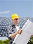 Portrait of mid adult italian male electrician reading blueprints in solar power station and smiling. Vertical shape, side view. Copy space