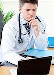 Worried male doctor using a laptop in his practice
