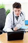 Confident male doctor using a laptop sitting at his desk in a practice