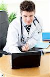 Assertive male doctor using a laptop sitting at his desk in a practice