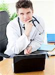 Smiling male doctor using a laptop sitting at his desk in a practice