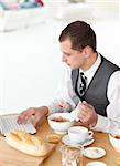 Young businessman using a laptop while having breakfast at home