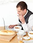 Charming businessman using a laptop while having breakfast at home