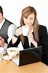 Serious businesswoman using a laptop while having breakfast at home