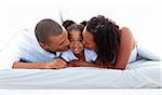 Cheerful parents kissing their daughter lying on a bed