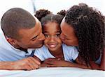 Loving parents kissing their daughter lying on a bed