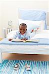 Smiling little boy reading a book lying on his bed