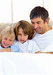 Attentive father and his children reading book lying in bed