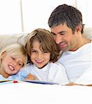 Close-up of father and his children reading book lying in bed