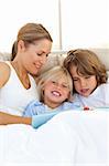 Pretty mother and her children reading book lying in bed