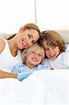 Beautiful mother and her children reading book lying in bed