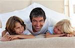 Smiling father talking with his children lying on bed at home