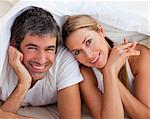 Enamoured couple having fun lying on bed at home