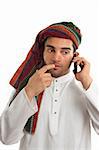 Pondering arab ethnic middle eastern businessman dressed in traditional clothing.   He is using a mobile cellphone. White background.