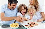 Excited children eating a pizza with their parents in the living-room