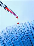 Close up of a pipette dropping a red sample into a test tube.