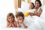 Happy siblings having breakfast with their parents lying on the bed