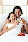 Happy couple drinking Champagne with strawberries on the bed
