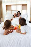 Happy family having breakfast lying on the bed together