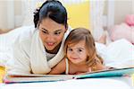 Cute little girl reading a book with her mother in the bedroom