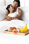 Smiling lovers having breakfast on the bed together
