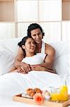 Young lovers having breakfast lying on the bed