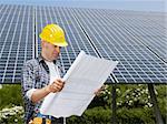 Portrait of mid adult italian male electrician reading blueprints in solar power station and smiling. Horizontal shape, side view. Copy space