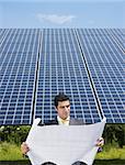 Portrait of mid adult italian male engineer reading blueprints in solar power station and smiling. Vertical shape, front view. Copy space