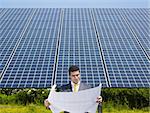 Portrait of mid adult italian male engineer reading blueprints in solar power station and smiling. Horizontal shape, front view. Copy space