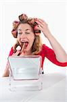 middle-aged woman with hair rollers eating cake looking at mirror