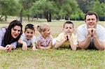 Cheerful family of five lying on lawn in the green park and looking at you