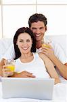 Smiling couple drinking orange juice lying in the bed