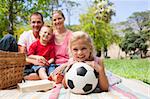 Little blond girl holding a soccer ball at a picnic with her family