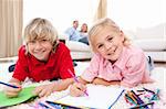 Happy siblings drawing lying on the floor in the living-room