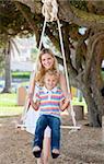 Caring mother pushing her daughter on a swing in a park