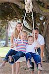 Joyful parents pushing their children on a swing in a park