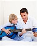 Smiling little boy playing guitar with his father in the bedroom