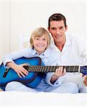 Merry little boy playing guitar with his father in the bedroom