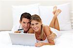 Cheerful couple shopping online lying on their bed