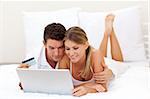 Smiling couple shopping online lying on their bed