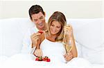 Lovers drinking Champagne with strawberries lying on their bed