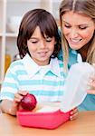 Smiling little boy and his mother preparing his snack in the kitchen