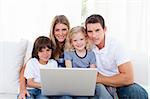 Portrait of a joyful family using a laptop sitting on sofa at home